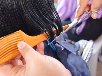 Cropped hands of barber cutting woman hair in salon