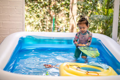 Cute little girl playing in an inflatable rubber swimming pool at home during quarantine period.