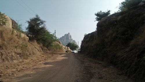 Dirt road amidst trees against clear sky