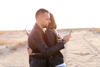 Side view of couple using smart phones while embracing at beach