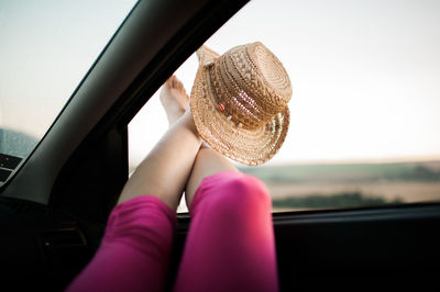 Low section of woman with hat resting in car against sky