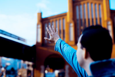 Man with hand raised standing against building in city