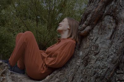 Side view of young woman looking at tree trunk