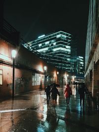 People walking on wet illuminated city at night