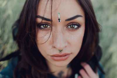 From above close up portrait of tranquil stylish female with tattoo and bindi looking at camera with curiosity on street blurred background