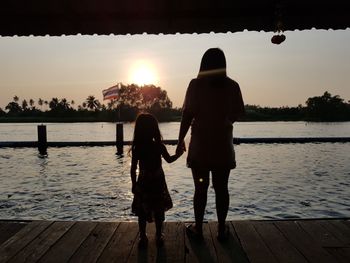 Rear view of women walking on lake against sky during sunset