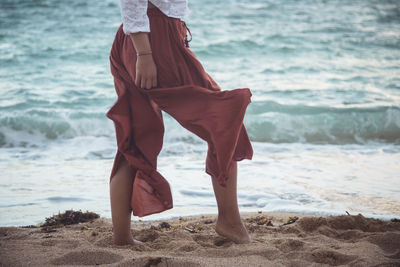 Low section of young woman standing at beach