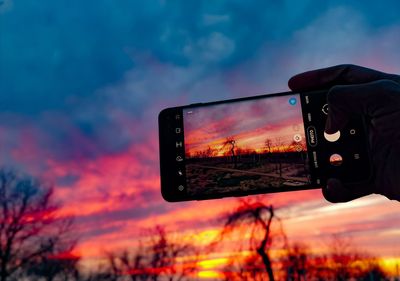 Person photographing through smart phone against sky during sunset