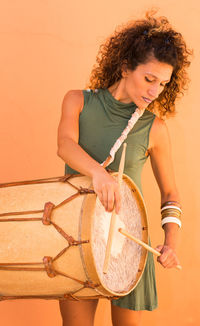 Woman playing drum standing against wall