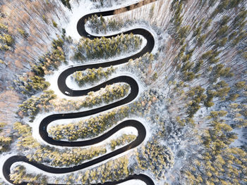 Curvy windy road in snow covered forest, top down aerial view