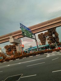 Road sign by street against sky in city