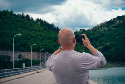 Rear view of man photographing through mobile phone against sky