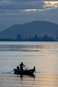 Man on boat in sea against sky during sunset