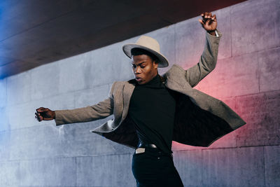 Young man looking away while standing against wall