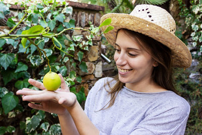 Close-up of smiling woman looking at lemon growing on plant