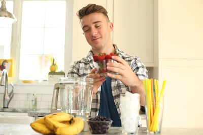 Smiling young man holding ice cream at home