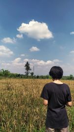 Rear view of man standing on field against sky