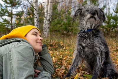 Smiling woman wearing knit hat sitting with dog in forest