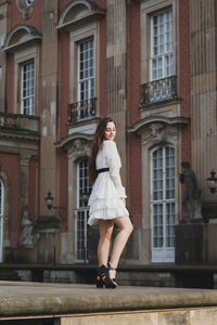 Full length portrait of woman standing against building