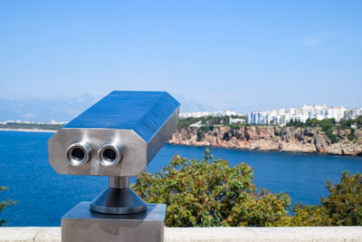 Close-up of coin-operated binoculars by sea against clear blue sky