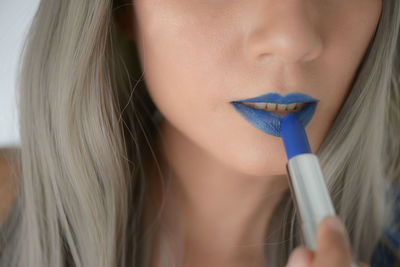 Close-up of beautiful woman applying blue lipstick