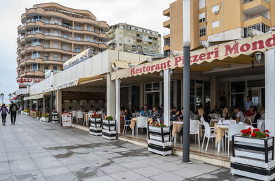 People on sidewalk cafe by buildings in city