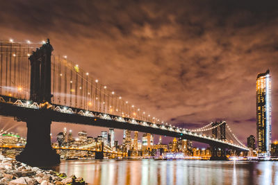 Low angle view of illuminated bridge over river in city at night