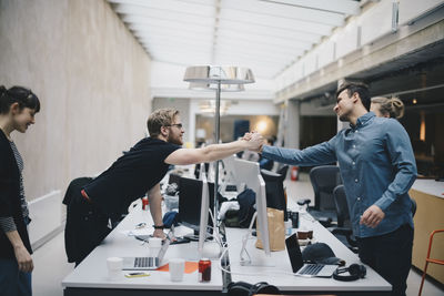 Male computer programmers holding hands over desk in office