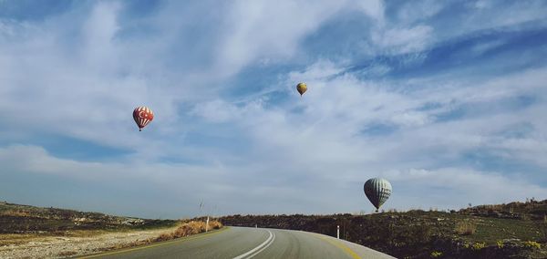 Hot air balloons flying over road against sky