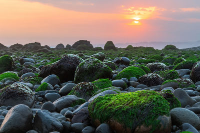 Rocks at sea shore against sky during sunset