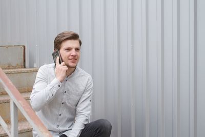 Smiling young man answering mobile phone while sitting on stairs