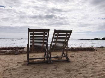 Empty chairs on beach against sky