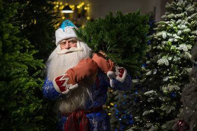 Portrait of santa clause standing amidst christmas tree