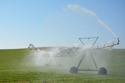 Agricultural sprinkler spraying water on field against sky