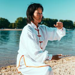 Woman practicing martial arts at lake against sky