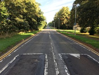 Empty road amidst trees against sky