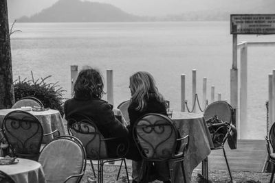 Rear view of people sitting on chair by sea