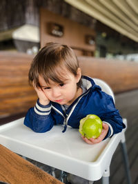 Boy toddler holding apple in his hand and sitting thoughtfully