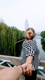 Rear view of woman with arms outstretched against river