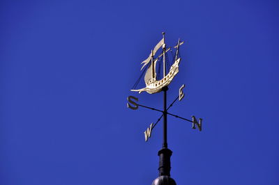 Low angle view of weather vane with ship sculpture against clear blue sky