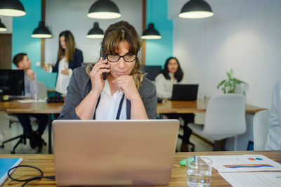 Businesswoman talking on phone while looking at laptop