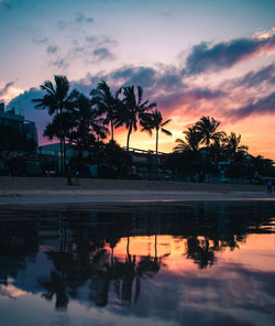 Silhouette palm trees by swimming pool against sky during sunset