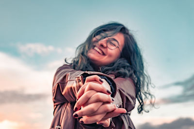 Portrait of a smiling young woman using smart phone against sky