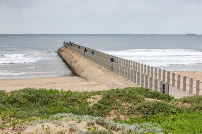 People on pier at beach against sky