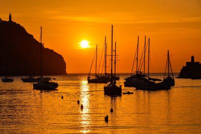 Silhouette boats moored in sea against orange sky during sunset