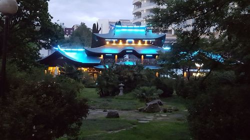 Illuminated park by buildings against sky at night