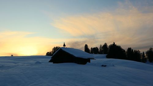 Built structure on snow covered field against sky during sunset