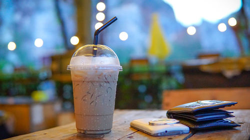 Close-up of iced coffee by mobile phone and wallet on wooden table in restaurant