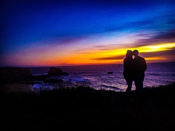 Rear view of silhouette man standing at beach during sunset