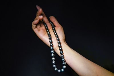 Cropped hand of woman with chain against black background